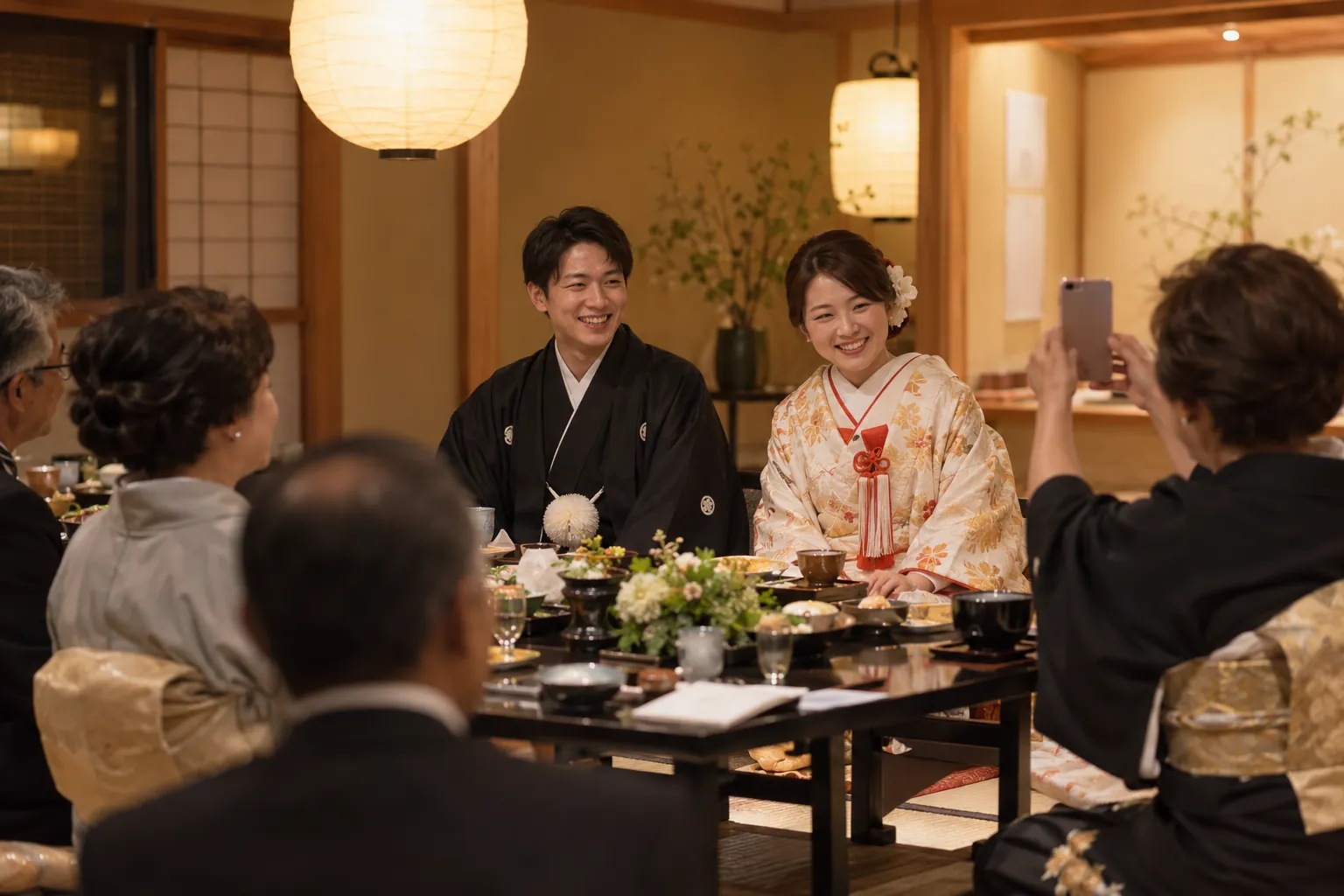 和食店の個室で、着物姿の新郎新婦を親族がスマートフォンで撮影している様子