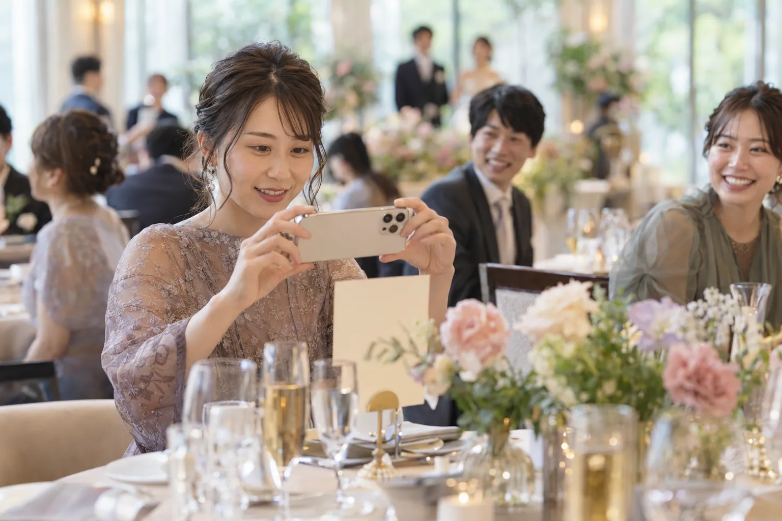 披露宴の円卓でスマートフォンを構えるゲストと、手前の小さなテーブルカード(イメージ写真)